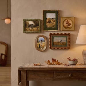 May include: A gallery wall arrangement featuring five framed artworks. The collection includes two rectangular frames with beaded edges, one oval gold frame, one square gold frame, and one rectangular frame with a large wooden beaded border.