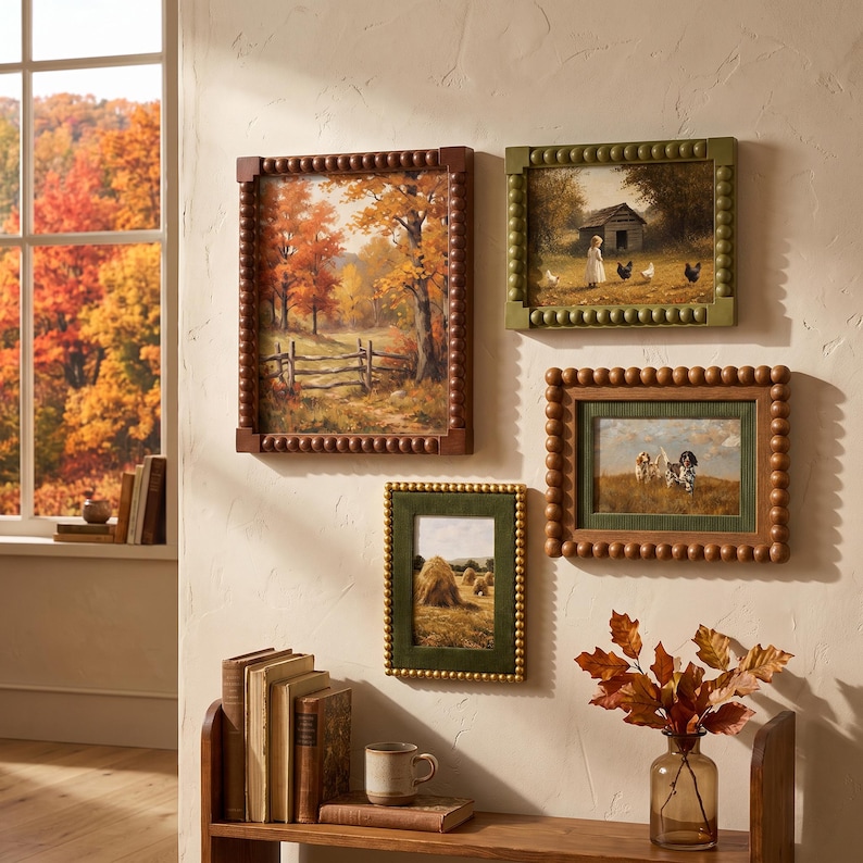 May include: Four rectangular wall frames with beaded edges displaying landscape and animal art. The frames are in shades of brown and olive green. Below, a wooden shelf holds stacked books, a ceramic mug, and a glass vase with autumn leaves.
