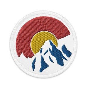 May include: Embroidered patch featuring a stylized mountain range with a red, yellow, and white sun rising behind it. The patch is white with a white border.