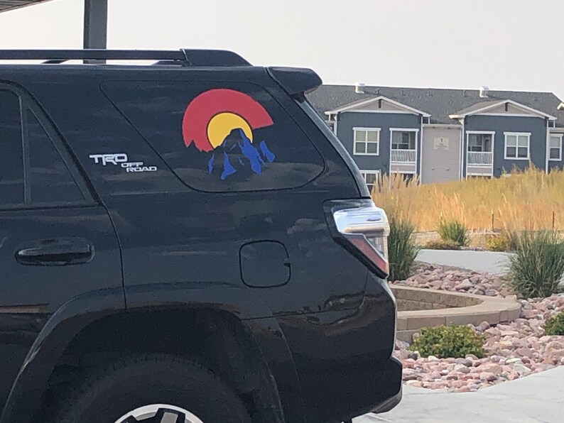 May include: Black SUV with a Colorado license plate sticker on the back window. The sticker features a red, yellow, and blue mountain scene with the text "Colorado" in white.