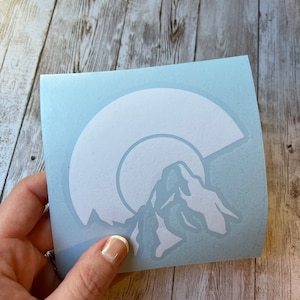 May include: White vinyl sticker with a mountain range silhouette and a crescent moon design. The sticker is on a light blue background.