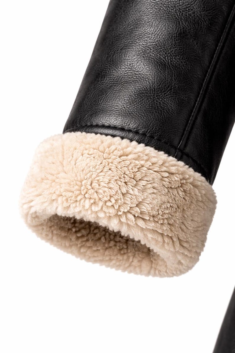 May include: Close-up of a black leather jacket sleeve with a beige, fluffy, faux fur lining at the cuff. The jacket appears to be made of a smooth, durable material, and the fur adds a contrasting texture.