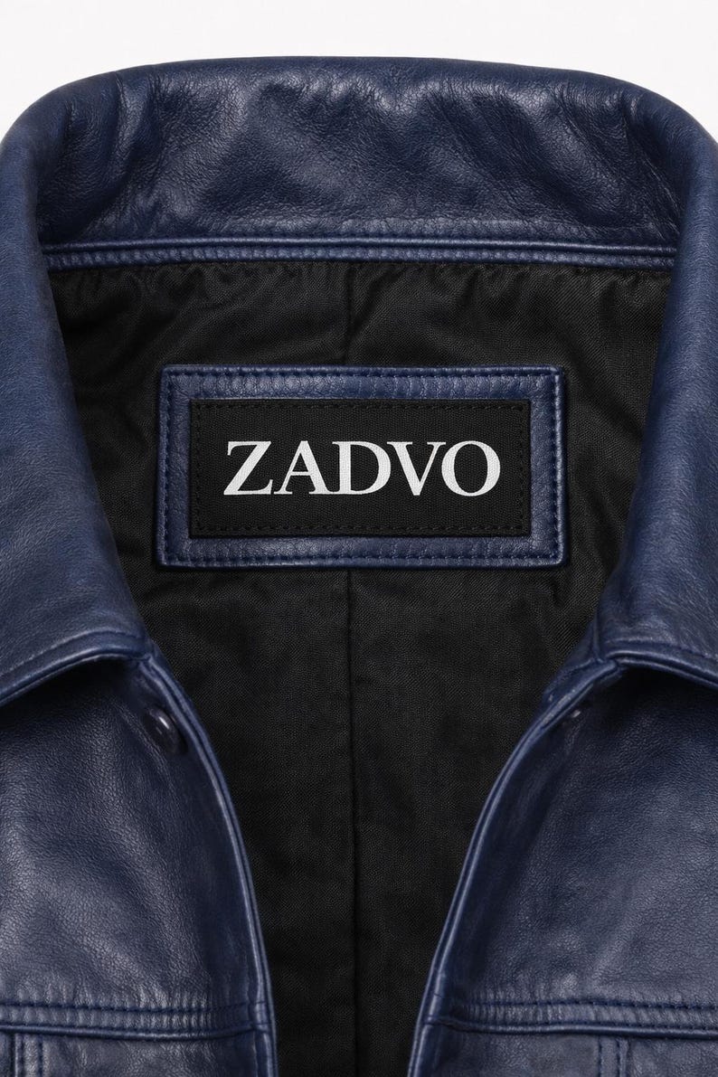May include: Close-up of a navy blue leather jacket collar. The jacket has a black interior lining and a label with the white text "ZADVO". The leather has a textured appearance.