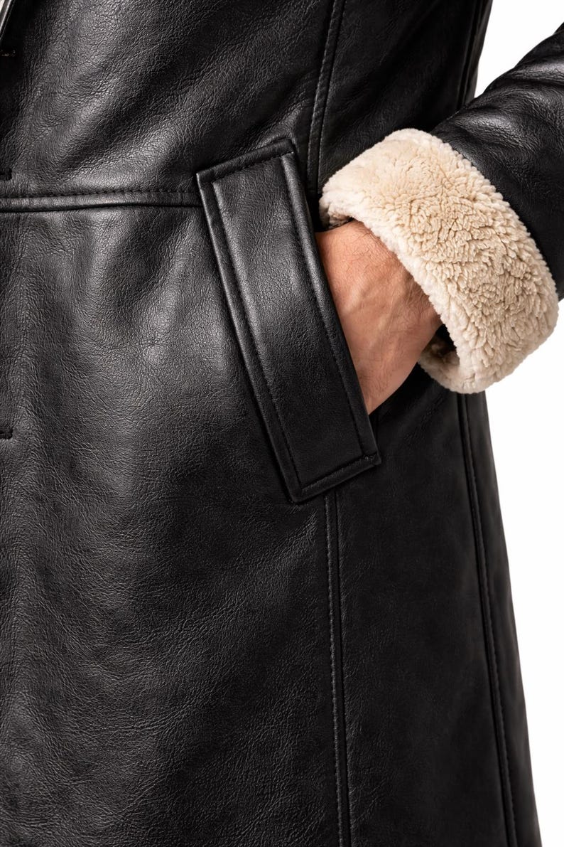 May include: Close-up of a black leather coat with a pocket and a tan, fuzzy lining on the sleeve cuff. The coat has a classic design and appears to be made of high-quality materials. The focus is on the texture and details of the coat.