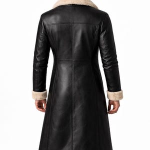 May include: Black leather coat with a cream-colored shearling collar and cuffs. The long coat features a tailored fit with vertical seams and a flared skirt. A classic outerwear piece.