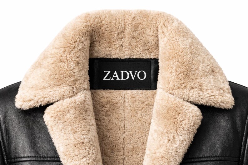 May include: Close-up of a black leather jacket with a beige shearling collar and lining. The brand name "ZADVO" is displayed on a black label on the collar.