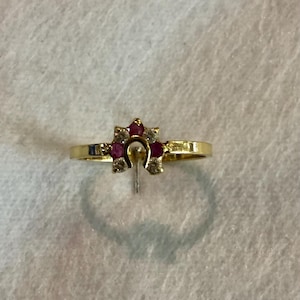 Puede incluir: Un anillo de oro con un diseño en forma de herradura. El anillo presenta un grupo de pequeñas piedras preciosas rojas redondas y piedras preciosas claras. El anillo está engastado en una fina banda de oro.