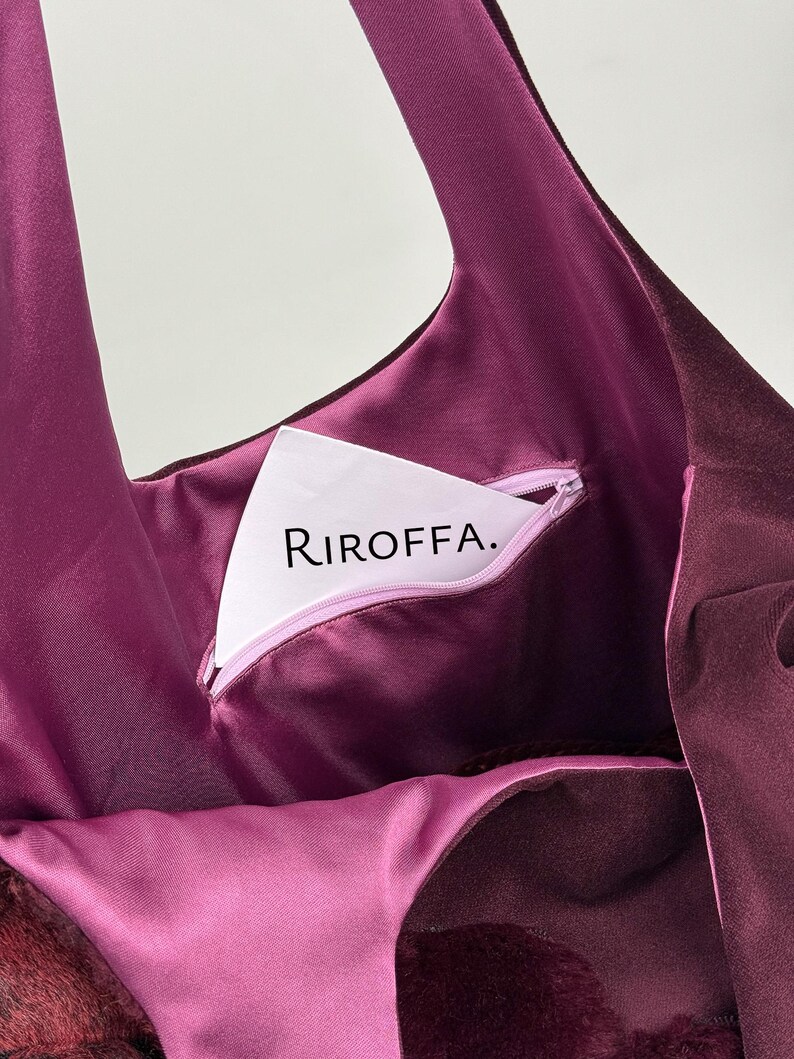May include: A close-up of a deep purple tote bag with a matching interior. The bag features a zippered pocket with the text "RIROFFA." The bag's interior is a lighter shade of purple, and the exterior has a velvety texture.