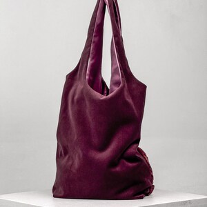May include: A deep burgundy velvet tote bag with a contrasting pink satin lining. The bag has long handles and a soft, unstructured shape, perfect for carrying essentials. The bag is displayed on a white surface against a neutral background.