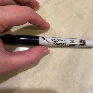 May include: A black and white permanent marker with the brand name "Sharpie" and the text "Fine Point Permanent Marker" printed on the side.