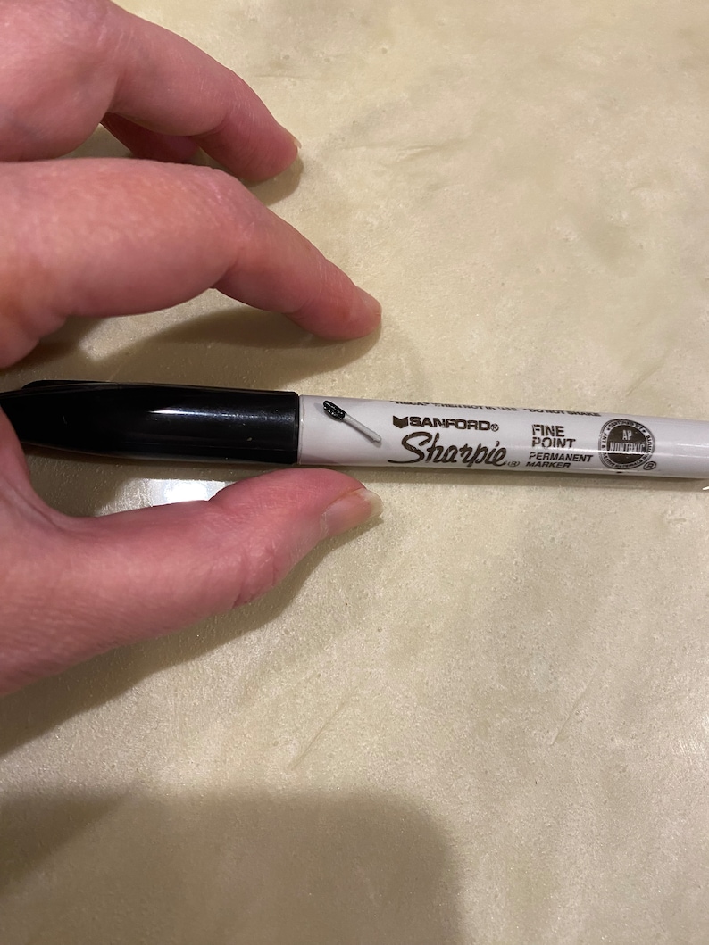 May include: A black and white permanent marker with the brand name "Sharpie" and the text "Fine Point Permanent Marker" printed on the side.