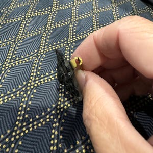 May include: A black and gold brooch with a floral design. The brooch has a pin on the back.