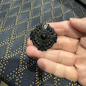 May include: A black jet brooch with a detailed design and a central round cabochon.