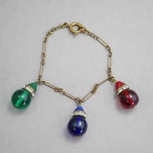 May include: A gold chain bracelet with three teardrop-shaped glass beads. The beads are green, blue, and red.