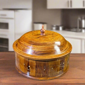 May include: A round wooden container with a domed lid and a small pointed finial handle. The exterior features a polished brown wood grain finish with thin, delicate brass wire inlay patterns forming floral and vine motifs around the sides.