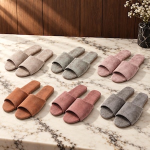 May include: Six pairs of open-toe slippers in various colors including beige, sage green, dusty rose, tan, mauve, and charcoal gray. Each pair features a wide, solid-colored fabric strap across the top and a flat, matching sole for indoor wear.