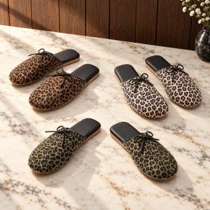 May include: Three pairs of slip-on slippers featuring leopard print patterns in brown, cream, and olive green. Each slipper has a black footbed, a rounded toe, and a decorative black bow detail on the upper section of the fabric exterior.