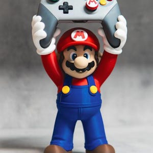 Op de afbeelding: Een Mario-figuur met een rode pet met een M, een rood shirt, een blauwe tuinbroek met gele knopen en bruine schoenen. Het figuur houdt een grijze gamecontroller boven het hoofd, voorzien van een groene L-knop, een rode M-knop en gekleurde knoppen.