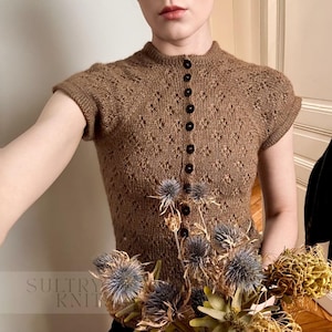 May include: A brown, short-sleeved knit top with a high neckline and a series of black buttons down the front. The top has a textured, openwork design. The text "SULTRY KNIT" is visible at the bottom left. The top is part of a clothing collection.