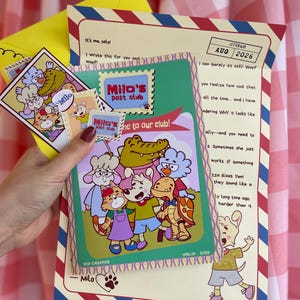 May include: A Milo's Post Club stationery set featuring a letter with red and blue border accents, a green card with a cartoon animal group illustration, and small stickers. The letter includes the text Milo's Post Club, AUG 2026, and Vol 01-2026.