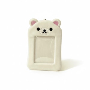 May include: A white, plush bear-shaped ID holder with a clear window. The bear has pink ears, black eyes, and a stitched black nose and mouth. The holder is rectangular with rounded edges and a small loop at the top.
