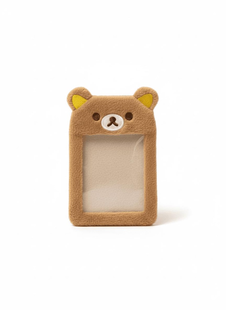 May include: A brown plush card holder shaped like a bear's face, with yellow accents on the ears. The card holder has a clear window for displaying a card or ID. The bear face has embroidered details.