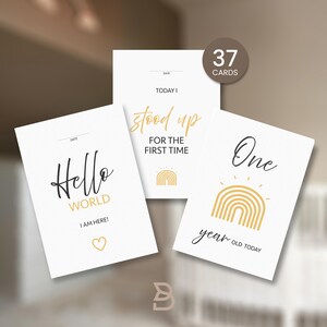 Könnte beinhalten: Ein Set von 37 Baby-Meilensteinkarten mit minimalistischen Designs. Die Karten zeigen Sätze wie "Hallo Welt", "Ein Jahr alt heute" und "stand zum ersten Mal auf". Die Karten haben einen weißen Hintergrund mit schwarzem und goldenem Text und Illustrationen.