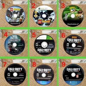 May include: A collection of nine circular video game discs for various consoles including PlayStation 2, PlayStation 3, PlayStation 4, and Xbox 360. The discs feature titles such as LEGO Batman, Ben 10 Protector of Earth, and Call of Duty Black Ops.