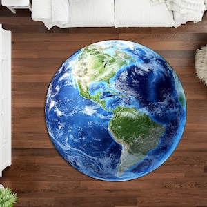 May include: A round area rug featuring a detailed depiction of Earth, showcasing continents in green and brown, surrounded by blue oceans and white cloud formations. The rug is placed on a dark wood floor.