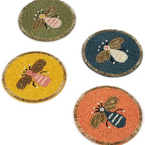 May include: Four beaded coasters with bee designs. The coasters are round and feature bees in shades of brown, pink, and white. The backgrounds are yellow, green, blue, and orange, with a gold border.