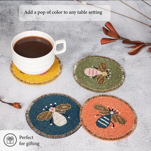 May include: A white coffee cup with dark liquid sits on a yellow beaded coaster. Three additional beaded coasters in green, blue, and orange feature bee designs. The text "Add a pop of color to any table setting" is visible. The text "Perfect for gifting" is also visible.