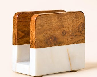 May include: A rectangular napkin holder featuring a two-tone design. The upper section is constructed from brown wood with a visible natural grain, while the lower section is made of smooth white marble with subtle grey veining throughout the base.
