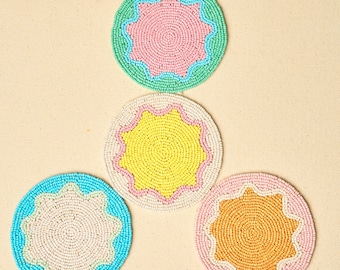 May include: Four circular coasters crafted from small glass beads. Each coaster features a central star-shaped pattern with scalloped edges. The colour combinations include mint green with pink, cream with yellow, bright blue with cream, and pink with orange.