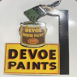 May include: A vintage-style metal sign featuring a hand holding a brush pouring green paint into a brown can labeled DEVOE HOUSE PAINT FOUNDED 1754. Below, a yellow rectangular section displays the text DEVOE PAINTS in bold black letters.