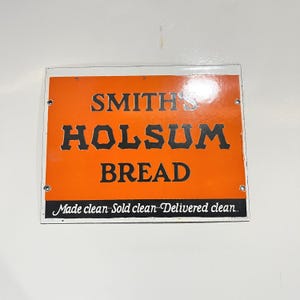 May include: Vintage orange and white metal sign for Smith's Holsom Bread. The sign features the text "SMITH'S HOLSUM BREAD" in bold black letters. Below the bread title, the sign reads "Made clean. Sold clean. Delivered clean."