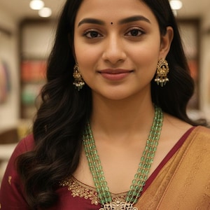 May include: A woman wearing a multi-strand green beaded necklace with a large, ornate pendant. The pendant features intricate detailing and is adorned with small white stones. She is also wearing matching earrings.