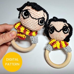 Puede incluir: Dos sonajeros de ganchillo para bebés, cada uno con la cara de un personaje con pelo negro, gafas y una bufanda amarilla y roja. Los sonajeros tienen anillos de madera y mangas grises. El texto "DIGITAL PATTERN" está en un círculo amarillo.
