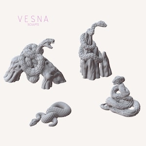 Op de afbeelding: Vier grijze slangenbeelden in verschillende poses. Eén slang is opgerold op een rots, een andere op een rotsformatie, en twee andere zijn opgerold. De tekst "VESNA SCULPTS" staat in de linkerbovenhoek.