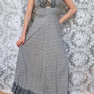 May include: A floor-length grey dress featuring a small repeating floral pattern, a fitted bodice with a lace-up front closure, wide shoulder straps, and a ruffled hemline at the bottom. The fabric has a textured appearance throughout the garment.