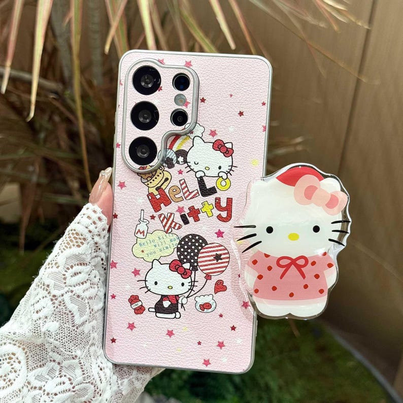 Peut inclure: Coque de t&eacute;l&eacute;phone rose avec un motif Hello Kitty. L'&eacute;tui pr&eacute;sente un motif d'&eacute;toiles r&eacute;p&eacute;t&eacute;es et des illustrations de Hello Kitty avec des ballons et du texte. Une poign&eacute;e de t&eacute;l&eacute;phone Hello Kitty assortie est attach&eacute;e.