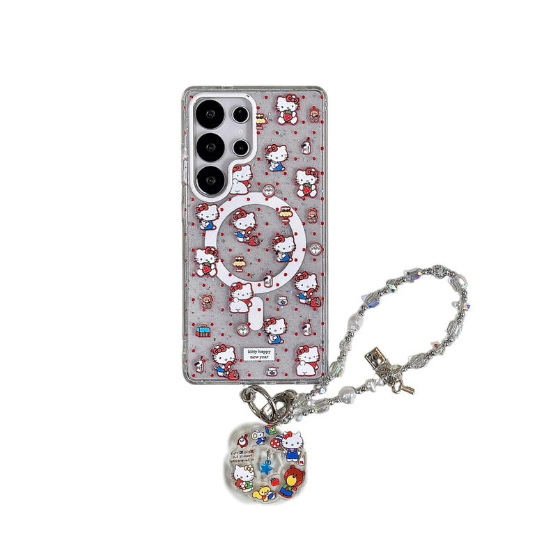 Może przedstawiać: Przezroczyste etui na telefon z motywami Hello Kitty i czerwonymi akcentami. Etui ma magnetyczny pierścień i napis "kitty happy new year". Widoczny jest r&oacute;wnież srebrny naszyjnik z koralik&oacute;w z zawieszką Hello Kitty.