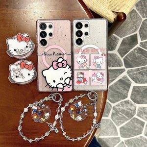 Peut inclure: Ensemble d'accessoires sur le th&egrave;me de Hello Kitty, comprenant deux coques de t&eacute;l&eacute;phone, deux supports de t&eacute;l&eacute;phone et deux porte-cl&eacute;s perl&eacute;s. Les coques de t&eacute;l&eacute;phone sont roses et transparentes, avec des graphismes Hello Kitty.