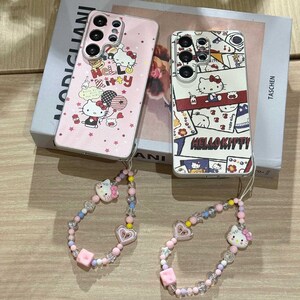 Peut inclure: Deux coques de t&eacute;l&eacute;phone avec des motifs Hello Kitty. L'une est rose avec des graphiques et du texte Hello Kitty, l'autre est blanche avec un collage d'images Hello Kitty. Deux bracelets de poignet assortis en perles avec des breloques Hello Kitty et des c&oelig;urs.