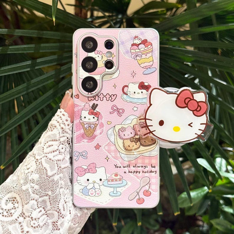 May include: Pink phone case featuring a cartoon cat design with a red bow. The case has illustrations of desserts and the text "You will always be a happy holiday." A matching cat-shaped phone grip is attached.