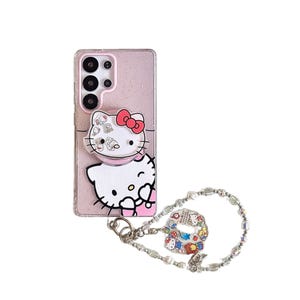 Peut inclure: Coque de t&eacute;l&eacute;phone rose paillet&eacute;e avec un motif Hello Kitty et un n&oelig;ud rouge. Comprend une poign&eacute;e pop-up et un bracelet &agrave; breloques avec un charm Hello Kitty. La coque est con&ccedil;ue pour un smartphone.