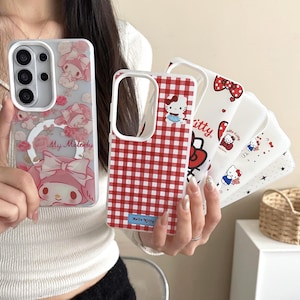 May include: A collection of phone cases featuring cartoon characters. One case has a red and white gingham pattern with a Hello Kitty graphic. Other cases display My Melody and Hello Kitty designs with bows and floral accents. The cases are white, pink, and red.