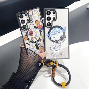 Könnte beinhalten: Zwei Handyhüllen mit Peanuts-Motiven. Eine Hülle hat einen schwarzen Rand und ein Design mit Snoopy und anderen Charakteren. Die andere Hülle hat einen schwarzen Rand und ein Design von Snoopy, der das Telefon mit dem Wort "RING!!" beantwortet.