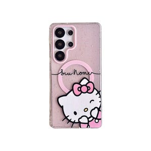Peut inclure: Coque de t&eacute;l&eacute;phone transparente avec un fond rose paillet&eacute; et un motif Hello Kitty. La coque pr&eacute;sente un cercle rose et le texte "Su Nome". Le graphisme Hello Kitty a un n&oelig;ud rose et tient un sac rose.
