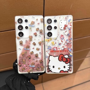 May include: Two clear phone cases with Hello Kitty designs. One case features Hello Kitty characters surfing and the other has a large Hello Kitty face with a red bow. Both cases have a glittery pink background.