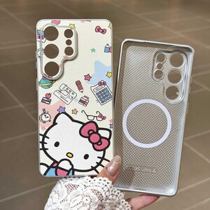 May include: A phone case featuring a Hello Kitty design with a pink bow, surrounded by colorful stars, pencils, and a calculator. The case is off-white with a matching silver-colored case next to it.